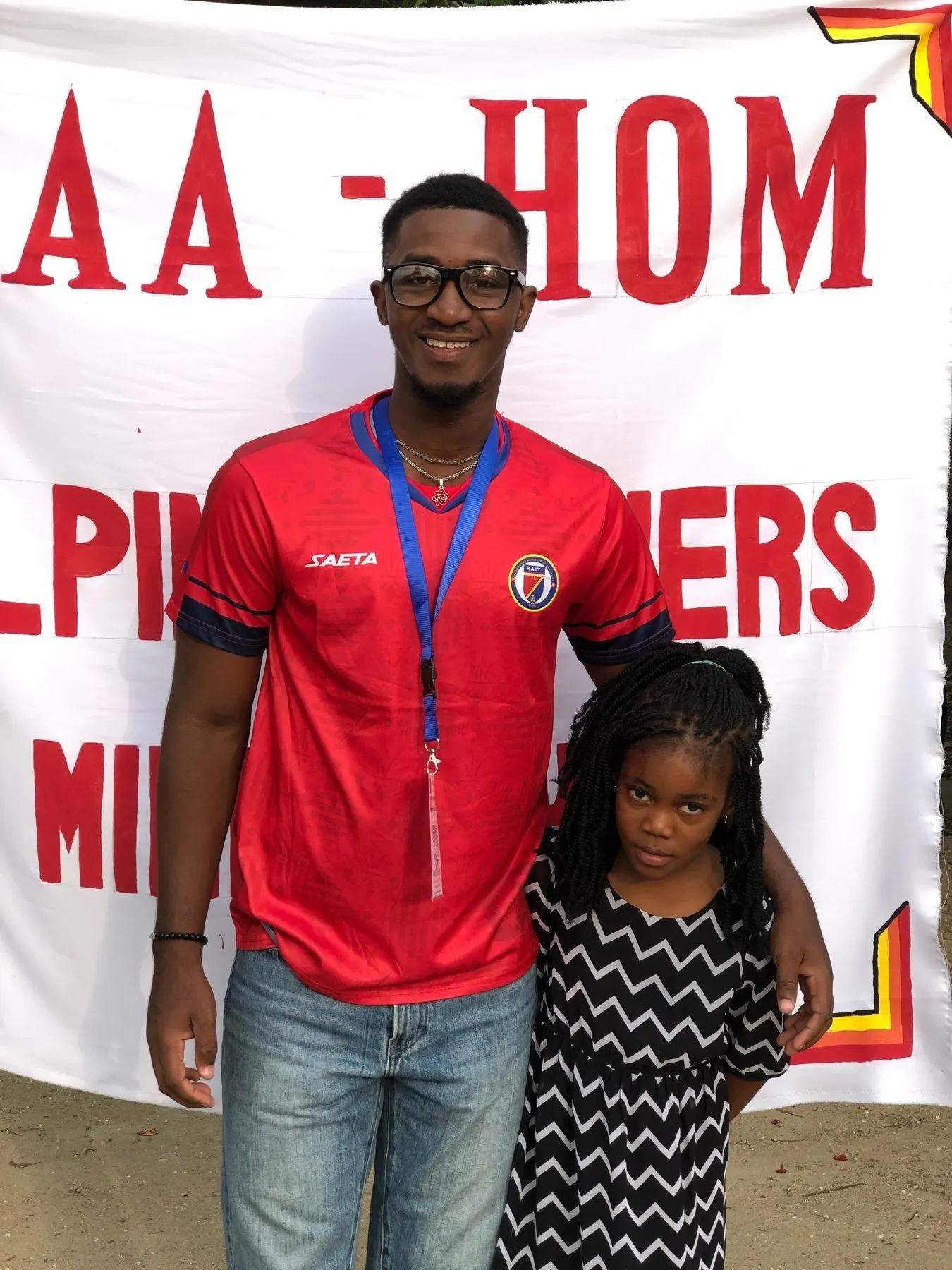 A young leader with his arm around a smiling child in front of a ministry banner