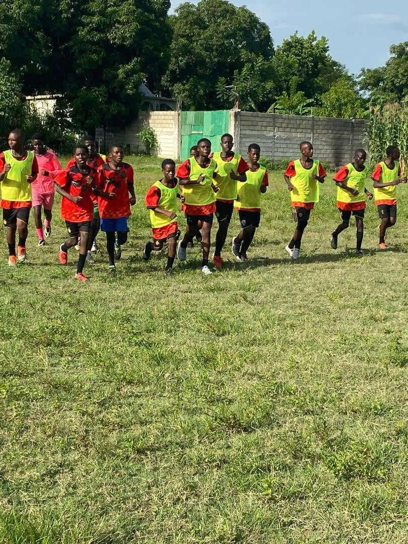 Young athletes in training bibs running laps on a grass field